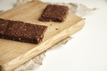 Close focus artisan organic freshly baked healthy chocolate bar with berries and grinded nuts on wooden board and craft paper, isolated on white table on side