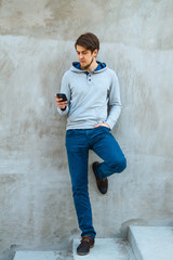 Obraz premium Young man writing sms standing by concrete wall. copy space