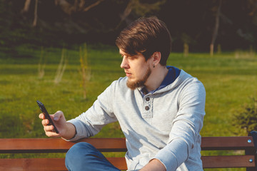 The young man in the park, sitting on a bench with phone