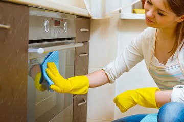 Cleaning the oven concept. Woman in gloves and an apron in the kitchen washing the oven door