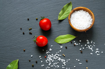 Food ingredients: tomatoes, bay laurel leaves and salt on black slate stone . Top view
