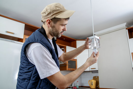 A male electrician fixing light on the ceiling. Worker changing a light bulb in the kitchen. Close-up.