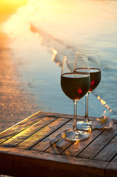 Romantic beach scene: two glasses of red wine at sunset near water