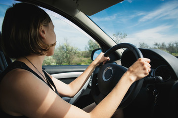Naklejka premium Young girl goes behind the wheel of the car and looks in the side mirror