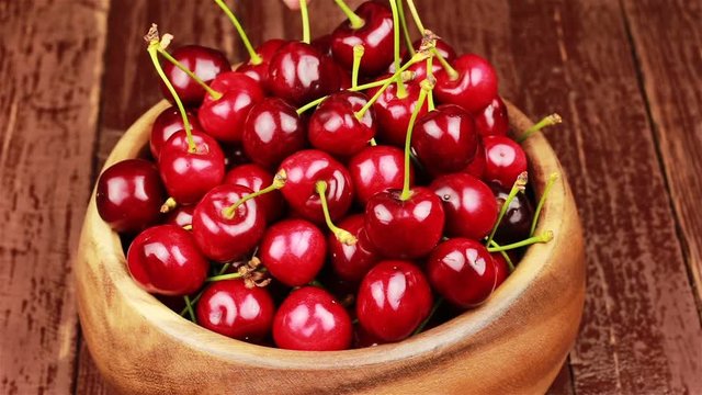 A man's hand take red ripe cherries in wooden bowl on wooden table