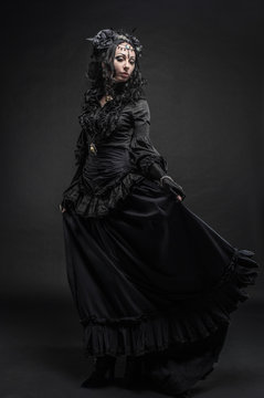 Fatal woman in vintage black dress posing on dark background