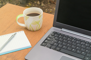 Cup of coffee with a laptop and a notebook on a wooden table.