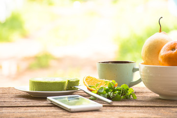 Background fruit in bowl and coffee cup with green tea cake and mint with smartphone.On wooden background outdoor view and holiday with relax