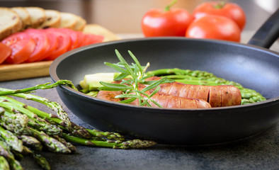 Fried sausages with asparagus, tomatoes and rosemary on a pan