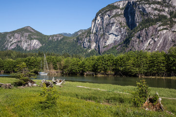 Sailboat parked at a river in Squamish with mountains in the background (Chief Mountain). Taken in Squamish, British Columbia, Canada on a sunny day.