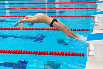 Young muscular swimmer jumping from starting block in a swimming pool