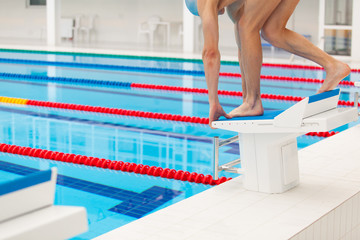 Young muscular swimmer in low position on starting block a swimming pool