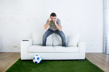 Foto auf Acrylglas football fan watching tv match on sofa with grass pitch carpet i © Wordley Calvo Stock