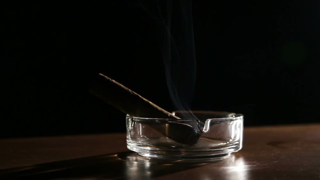 Burning cigar in ashtray.Smoking cigar in an ashtray on dark background