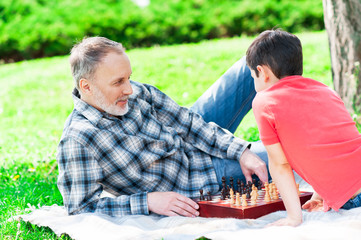 Cheerful mature man and his grandchild playing chess