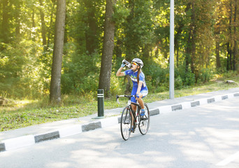 Naklejka premium Thirst. Female cyclist drinks water near bike