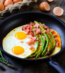 Fried eggs with asparagus and ham on a dark stone board