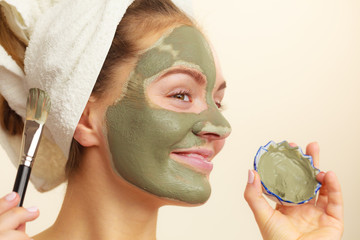 Woman applying with brush clay mud mask to her face