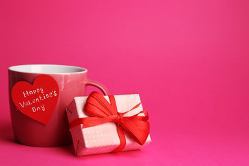 Cup with greeting card and gift box for Valentines Day on pink background