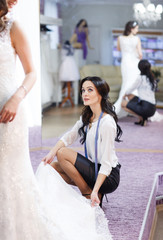 Female trying on wedding dress in a shop with women assistant.