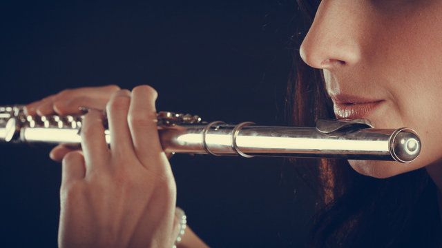 Woman playing transverse flute on black.