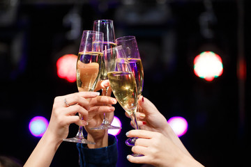 Clinking glasses of champagne in hands on bright lights backgrou