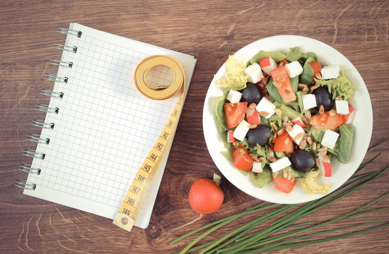 Vintage photo, greek salad with vegetables, centimeter and notepad for notes, healthy nutrition and slimming concept