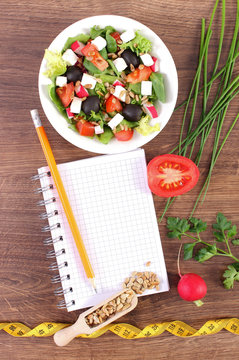 Fresh greek salad with vegetables, centimeter and notepad for writing notes, healthy nutrition and slimming concept