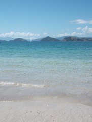 Clear blue sea, blue sky and white sand beach near Te Kouma - Coromandel Peninsula, New Zealand. A sailboat is in the distance.