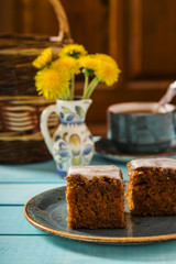 Carrot cake with cream cheese frosting on a turquoise plate and cup of tea on a turquoise wooden platform 