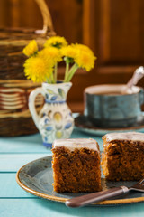Carrot cake with cream cheese frosting on a turquoise plate and cup of tea on a turquoise wooden platform 