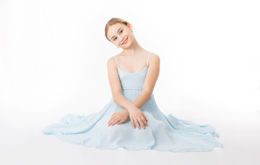 Fototapeta na wymiar Happy little girl in a blue dress is sitting on the floor on a white background