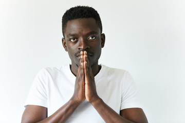 Close up portrait of handsome young African man praying isolated against white background. Dark...