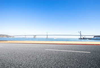 empty asphalt road near water and bay bridge in san francisco