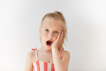 Blond European girl staring at the camera in white background. Amazed kid opening her mouth in...