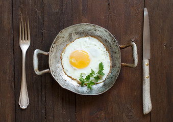 Fried egg in a old frying pan with fork and knife