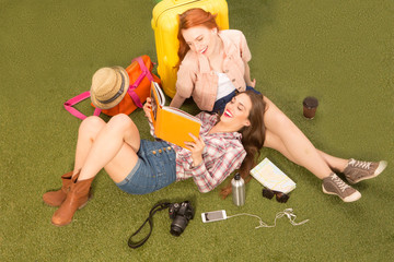 Naklejka premium Top view of cheerful beautiful tourist lady lying on green grass, communicating about places of sightseeing and looking at notebook.