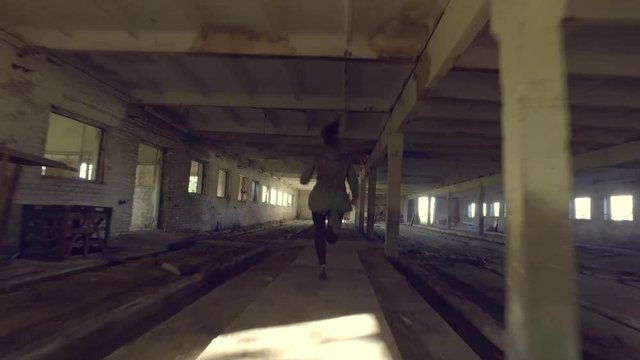 The girl run away from killer in abandoned building through the hallway. Back view horror dark mood. Steadicam shot. Smooth tracking. Old abandoned place. 