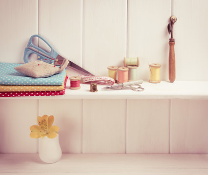 Set of tools for sewing and fabric lying on the wooden shelf.