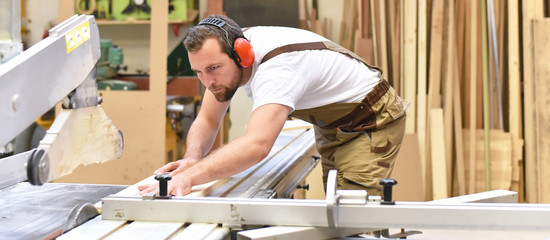 carpenter on a sawing machine // Tischler an einer Sägemaschine in einer Schreinerei - obrazy, fototapety, plakaty