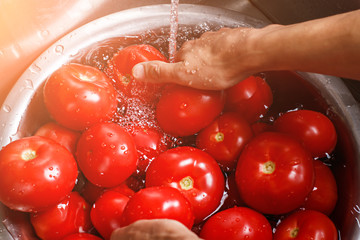 Male hands wash big tomatoes. Basin with tomatoes and water. Time to cook soup. Ripe and juicy.
