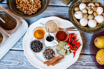 Pepper and bowl of eggs. Plate with spices beside walnuts. Curry and cinnamon sticks. Kaleidoscope of flavors.