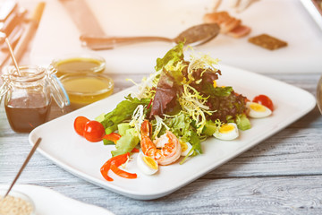 White plate with salad. Salad with shrimp and eggs. Frisee and cherry tomatoes. Natural food at local restaurant.