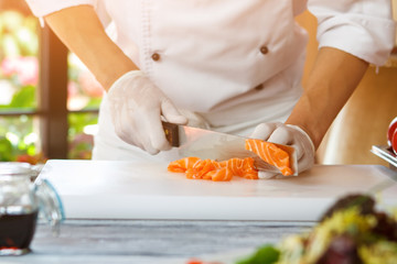 Hand with knife cutting fish. Red fish meat. Chef slices fresh salmon. Ingredient for seafood dish.