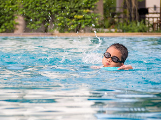 Asian boy swimming with the board in the pool