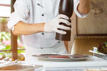 Man's hands with pepper dispenser. Piece of raw meat. Need to add some pepper. Chef prepares spicy duck meat.