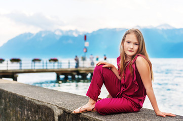 Fashion stylish portrait of pretty preteen girl of 8-9 years old, wearing maroon jumpsuit, posing by the lake