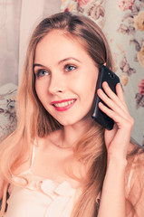 beautiful happy young blonde girl sitting on the couch talking on the phone, and smiling