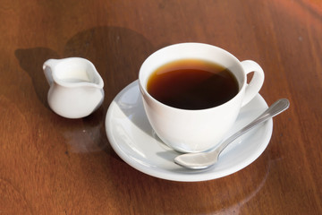 A cup of black coffee and milk on wooden table.