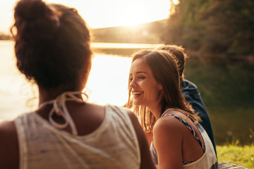 Happy young woman sitting by a lake with her friends